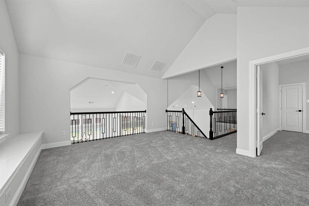 Vaulted ceilings, carpeted flooring, built-in window seating, and decorative black metal balustrade railings with pendant lighting