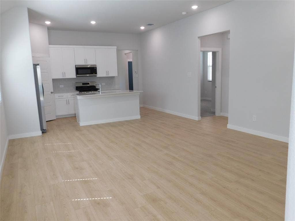 2702 Baynes Place, Princeton, TX 75407 Open-concept kitchen featuring white cabinetry, a peninsula, stainless steel appliances, and wood-finish flooring