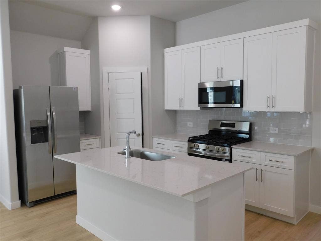 2702 Baynes Place, Princeton, TX 75407 Kitchen featuring white Shaker-style cabinetry, a central island with a stainless steel sink, stone countertops, stainless steel appliances, and subway tile backsplash