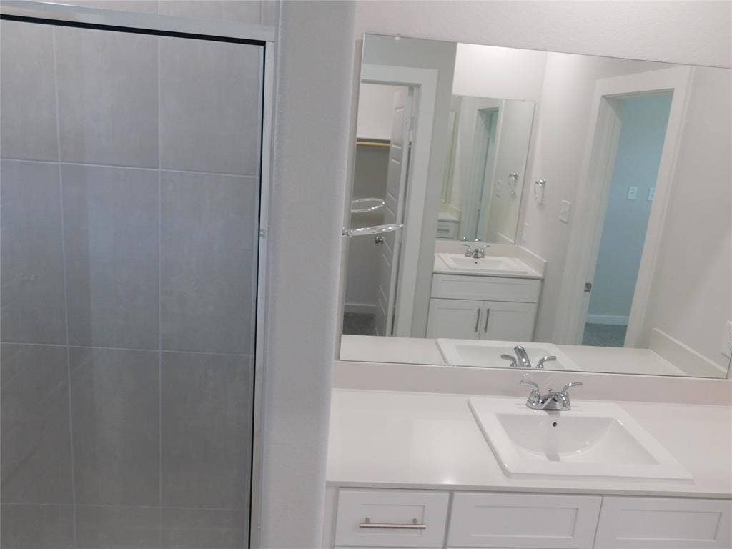 2702 Baynes Place, Princeton, TX 75407 Bathroom featuring a shower with tiled surround, white vanity with countertop sink, and a large wall-mounted mirror