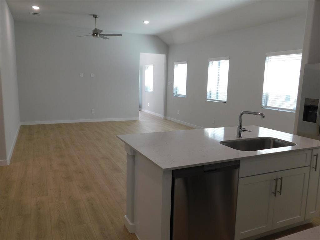 2702 Baynes Place, Princeton, TX 75407 Kitchen featuring a central island with a stone-composite countertop, stainless steel sink, and white cabinetry, complemented by wood-finish flooring, vaulted ceilings, and recessed lighting