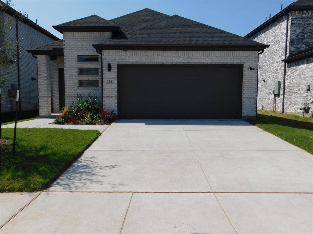 2702 Baynes Place, Princeton, TX 75407 Light-toned brick exterior featuring a multi-gabled roofline, concrete driveway, and triple-stacked horizontal windows