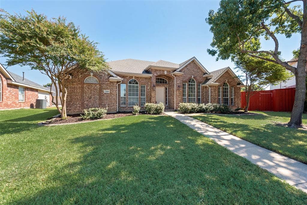 7900 Brookmount Street, Plano, TX 75024 Single-story brick exterior featuring an arched entryway, gabled rooflines, arched window detailing, and a manicured front lawn with mature landscaping