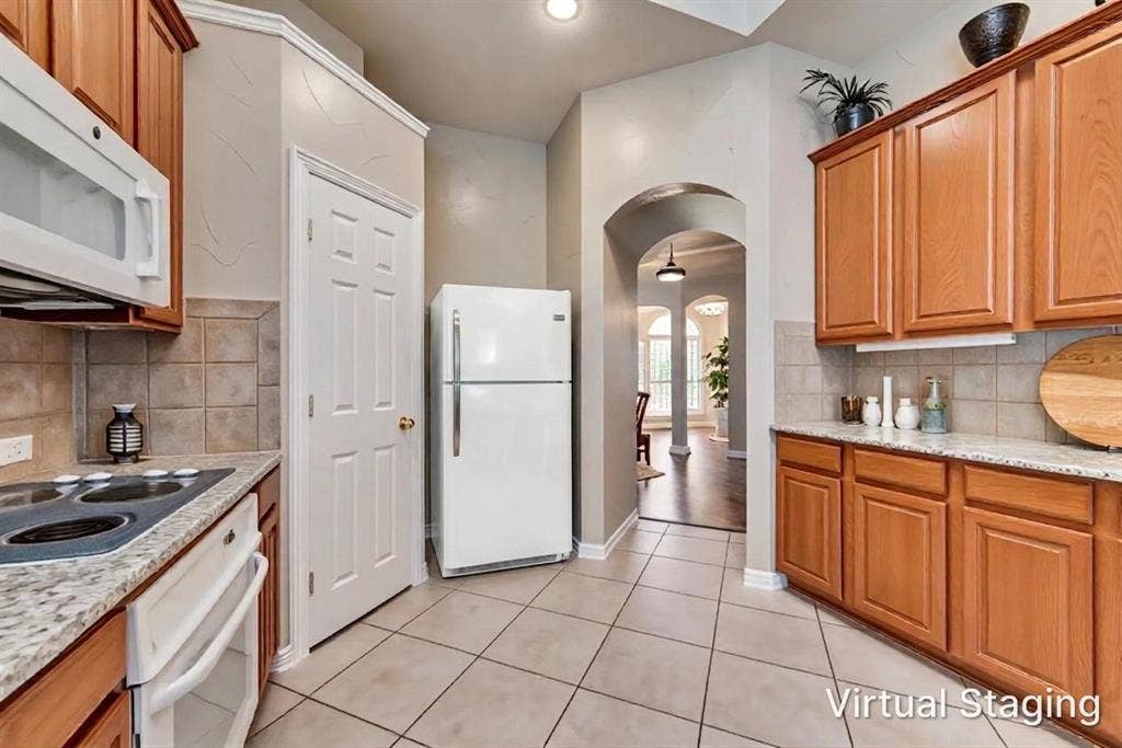 7900 Brookmount Street, Plano, TX 75024 Kitchen featuring wood cabinetry, stone-finish countertops, ceramic tile backsplash, built-in microwave, and arched entryway