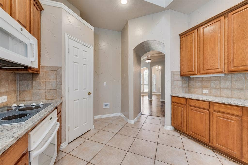 7900 Brookmount Street, Plano, TX 75024 Kitchen featuring wood cabinetry, stone countertops, square tile backsplash, built-in electric cooktop with over-the-range microwave, and ceramic tile flooring