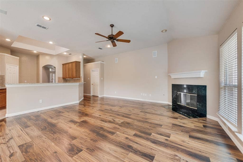 7900 Brookmount Street, Plano, TX 75024 Open living area featuring wood-finish flooring, high ceilings with a central ceiling fan, a corner fireplace with a stone-surround and mantle, and a breakfast bar with stone-finish countertops