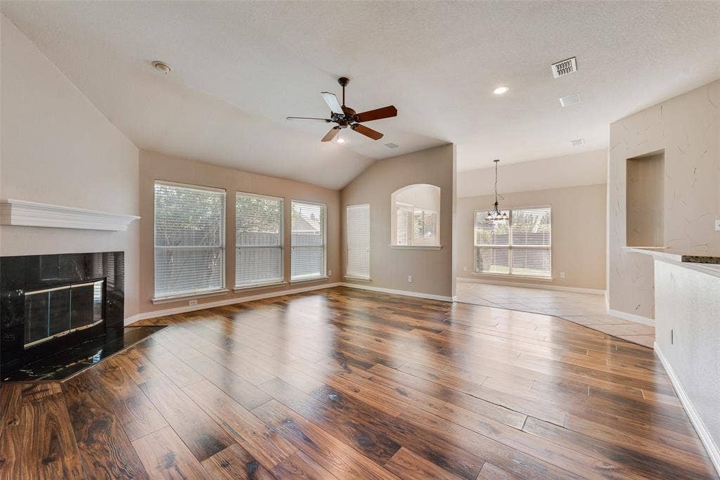 7900 Brookmount Street, Plano, TX 75024 Living area featuring vaulted ceilings, wood-finish flooring, a fireplace with a dark stone surround, a ceiling fan, and large windows
