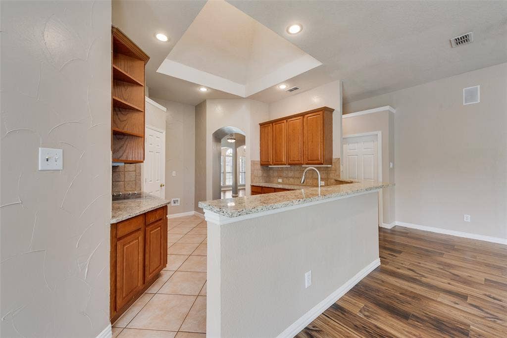 7900 Brookmount Street, Plano, TX 75024 Kitchen featuring a raised tray ceiling, wood-finish cabinetry, natural stone countertops, recessed lighting, and tile flooring