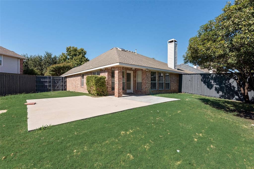 7900 Brookmount Street, Plano, TX 75024 Exterior rear elevation featuring a brick facade, chimney, concrete patio, and fenced perimeter