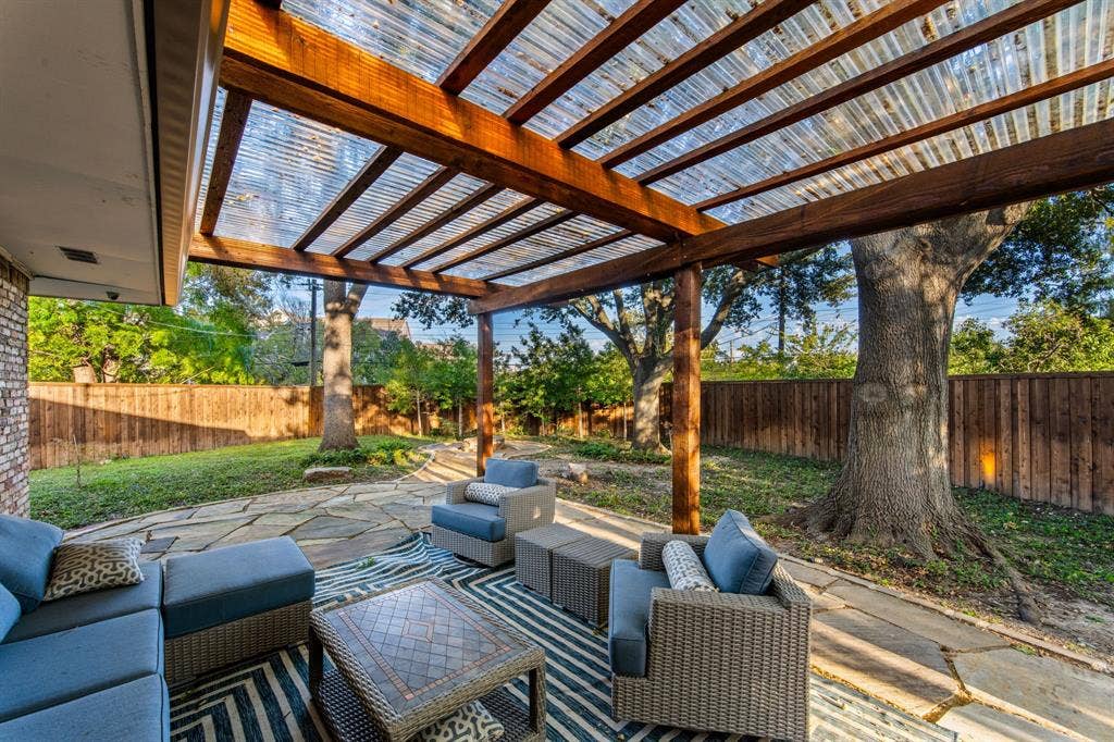 9656 Ravensway Drive, Dallas, TX 75238 Covered patio featuring a timber-frame pergola with a translucent corrugated roof, flagstone hardscaping, and a perimeter wood privacy fence
