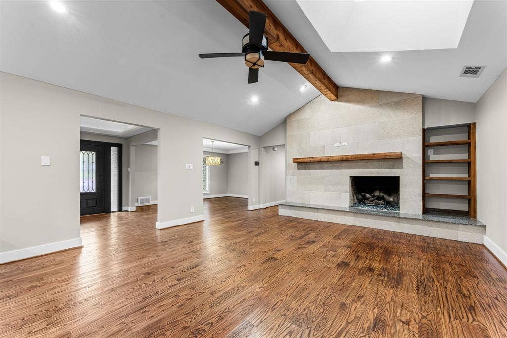 9656 Ravensway Drive, Dallas, TX 75238 Vaulted ceiling featuring a prominent wooden beam, stone fireplace with a wooden mantel and built-in shelving