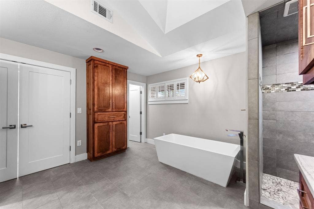 9656 Ravensway Drive, Dallas, TX 75238 Vaulted ceiling featuring a built-in wood cabinet, freestanding soaking tub and a tiled shower with stone-style flooring