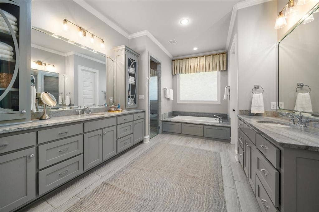 7609 Timber Trail, Tyler, TX 75703 Dual gray cabinetry vanities with stone countertops, undermount sinks, full-width mirrors, deep soaking tub, and tile flooring
