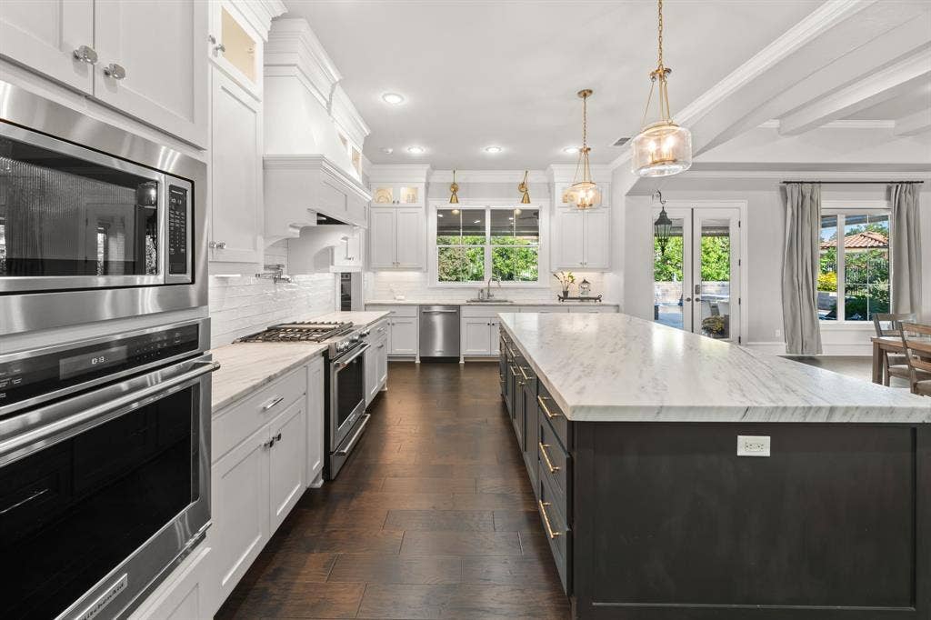 7609 Timber Trail, Tyler, TX 75703 Gourmet kitchen featuring a large central island with stone-finish countertops, custom cabinetry with brushed gold hardware, stainless steel appliances, and dark wood-finish flooring