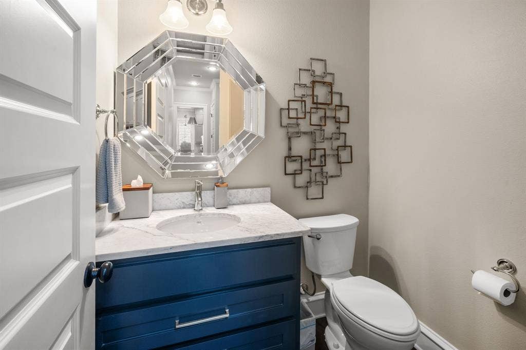 7609 Timber Trail, Tyler, TX 75703 Navy blue vanity with stone countertop, integrated sink, and chrome fixtures, paired with a multi-faceted octagonal mirror and dual-light wall sconce