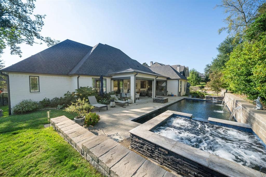 7609 Timber Trail, Tyler, TX 75703 Backyard featuring a covered patio, rectangular swimming pool with integrated water features, stone-finish spa, and tiered natural stone retaining walls