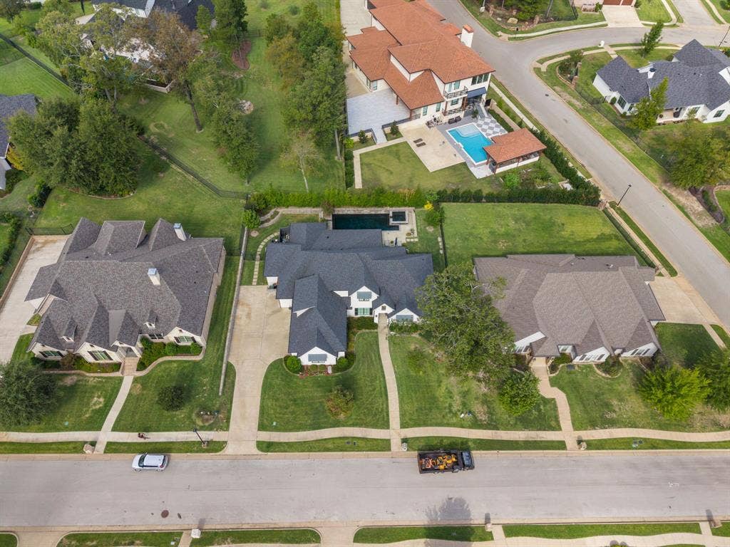 7609 Timber Trail, Tyler, TX 75703 Aerial perspective of a multi-gabled residence featuring a dark shingle roof, concrete driveway, stone-accented exterior, and a private rear swimming pool