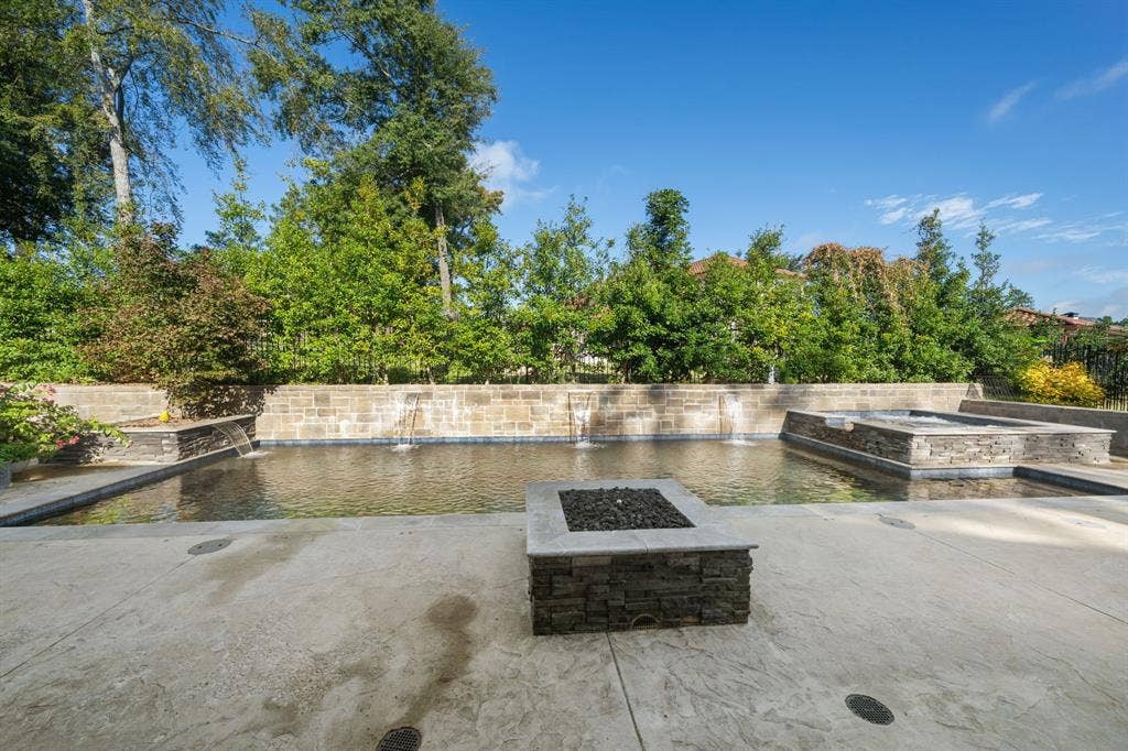 7609 Timber Trail, Tyler, TX 75703 Swimming pool with stone-veneer retaining wall and integrated water features, raised stone-clad spa, and square stone-top fire pit set within a stamped concrete deck