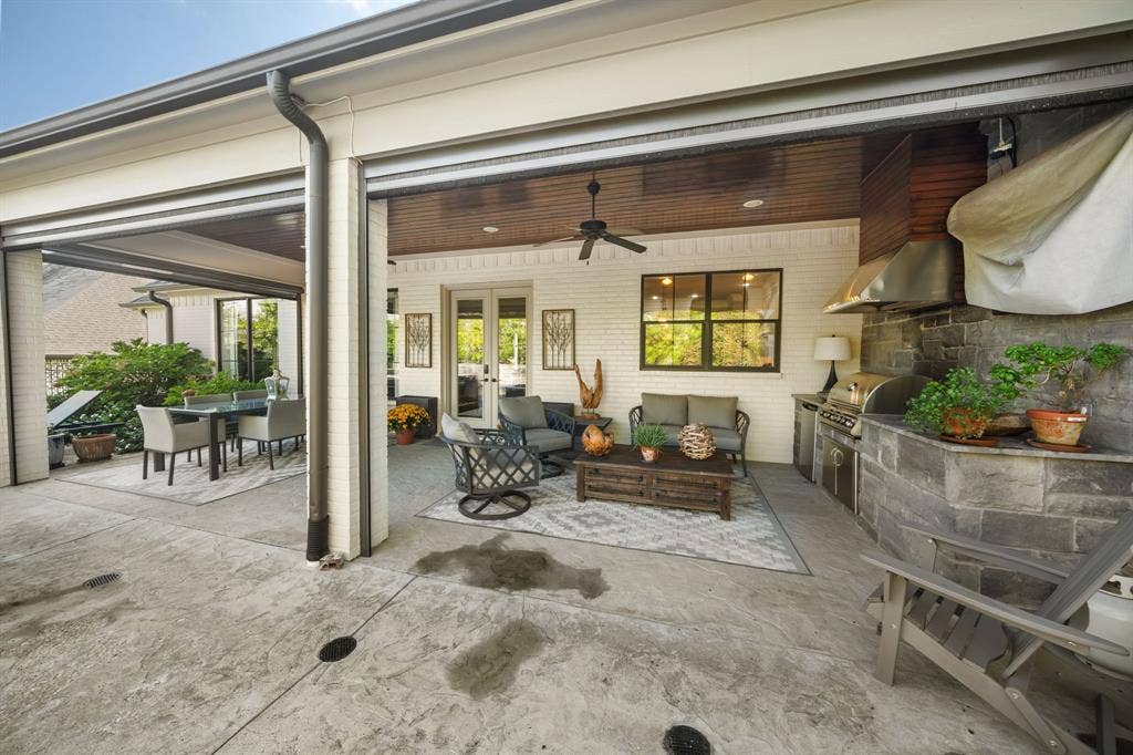 7609 Timber Trail, Tyler, TX 75703 Covered patio featuring a wood-plank ceiling, ceiling fan, built-in outdoor kitchen with a stainless steel vent hood, stone-veneer cooking station, and painted brick exterior walls
