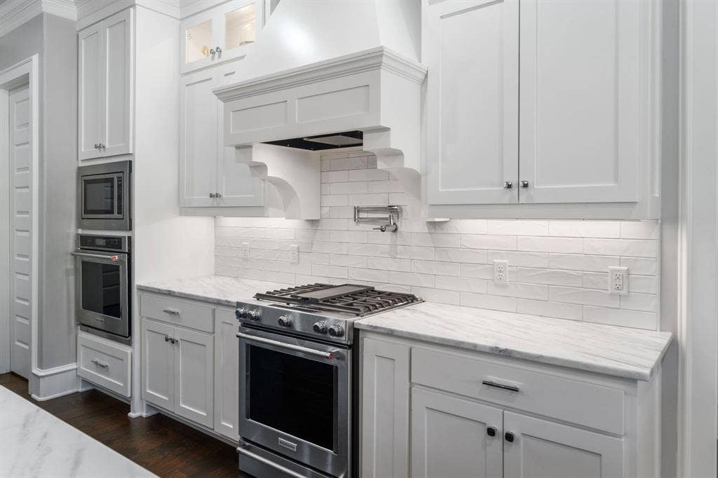 7609 Timber Trail, Tyler, TX 75703 Kitchen featuring white shaker-style cabinetry, natural stone countertops, subway tile backsplash, stainless steel gas range with a custom decorative vent hood, and built-in wall oven and microwave