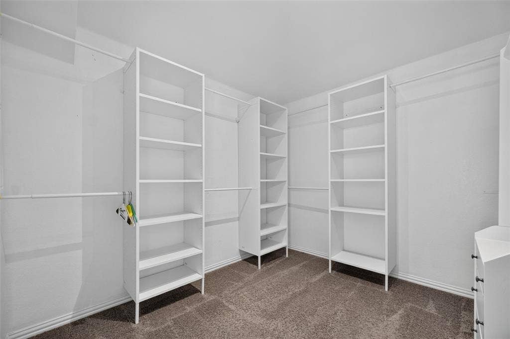 5726 Remington Drive, Garland, TX 75044 Walk-in closet featuring white built-in shelving units, multiple hanging rods, and neutral carpeting