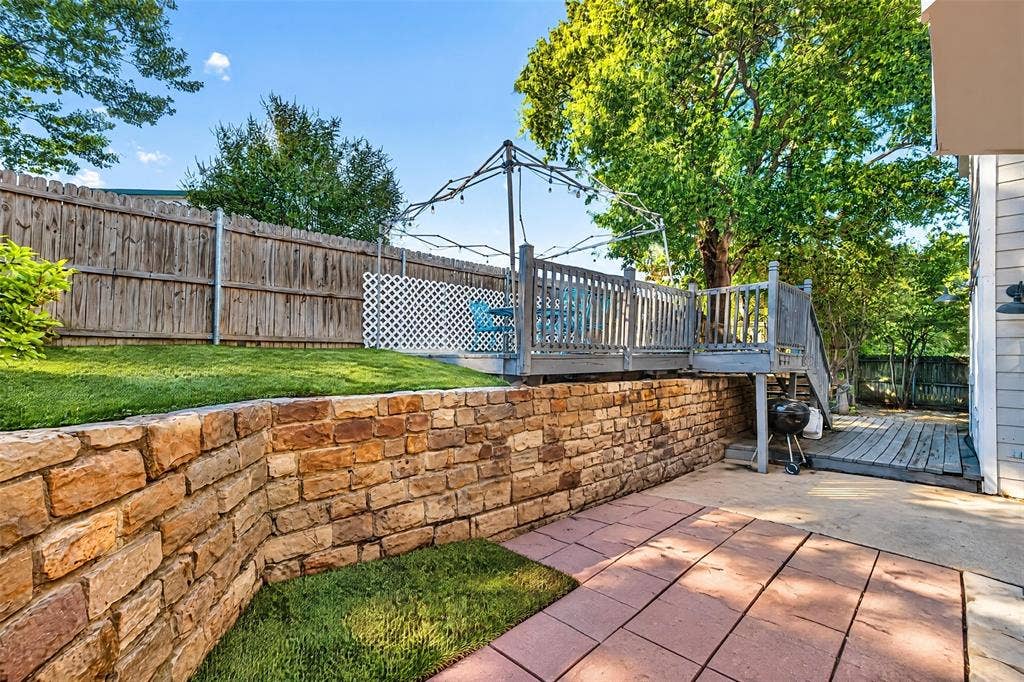 5726 Remington Drive, Garland, TX 75044 Tiered backyard featuring a stone retaining wall, paved patio area, raised wooden deck, and perimeter wood fencing