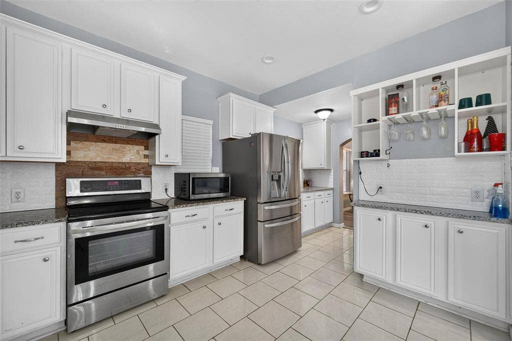 5726 Remington Drive, Garland, TX 75044 Kitchen featuring white shaker-style cabinetry, stainless steel appliances, speckled stone-finish countertops, textured brick-style backsplash, and ceramic tile flooring