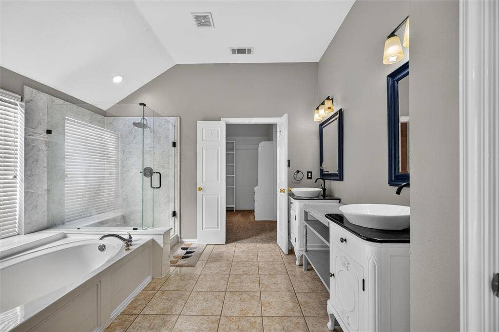 5726 Remington Drive, Garland, TX 75044 Dual vanities featuring white cabinetry, dark countertops, and vessel sinks, complemented by a glass-enclosed shower with stone-finish surround and a deep soaking tub