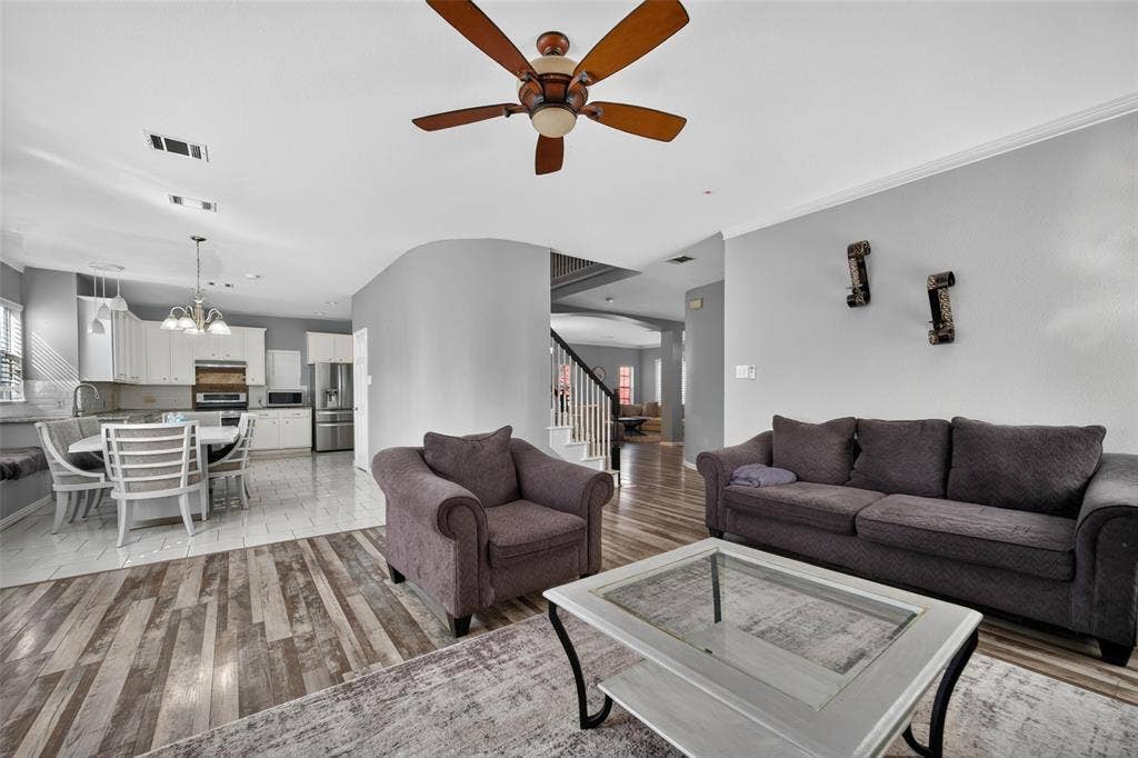 5726 Remington Drive, Garland, TX 75044 Open-concept interior featuring wood-finish flooring, a ceiling fan with integrated lighting, neutral wall paint, tile flooring in the kitchen area, and a curved architectural wall partition