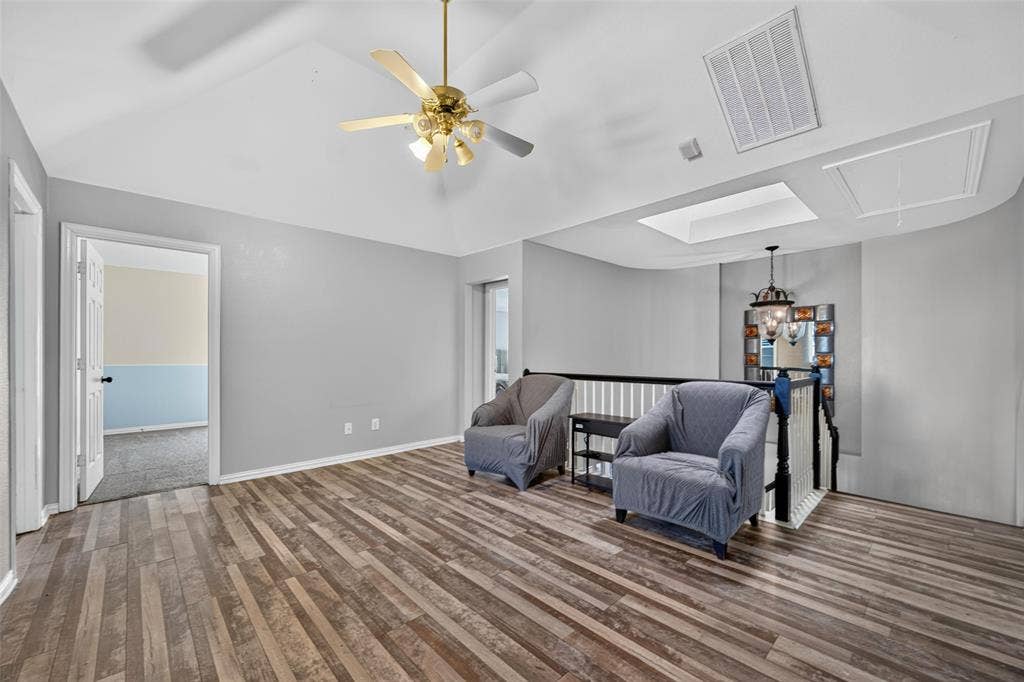 5726 Remington Drive, Garland, TX 75044 Vaulted ceiling with a centrally mounted ceiling fan, wood-finish flooring, integrated skylight, and a decorative staircase railing with a hanging pendant light