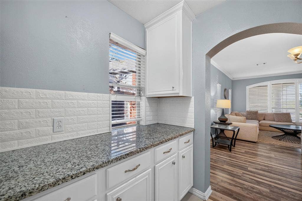 5726 Remington Drive, Garland, TX 75044 Kitchen featuring stone-finish countertops, white cabinetry, textured tile backsplash, and wood-finish flooring, accented by an architectural archway