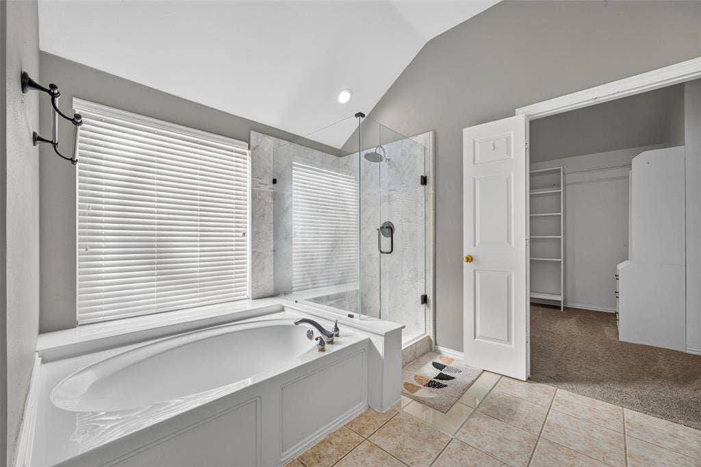 5726 Remington Drive, Garland, TX 75044 Bathroom featuring a vaulted ceiling, soaking tub with a deck mount faucet, walk-in glass-enclosed shower with stone-surround tile, and ceramic tile flooring