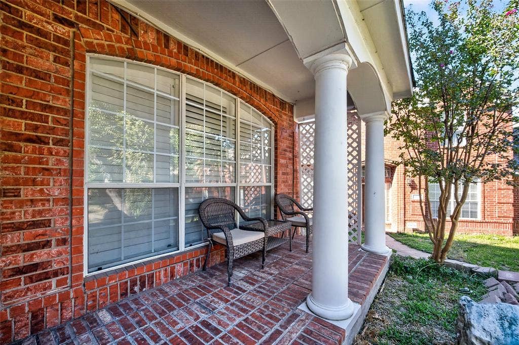 5726 Remington Drive, Garland, TX 75044 Covered brick porch featuring structural columns, decorative lattice screening, and multi-pane windows with brick trim