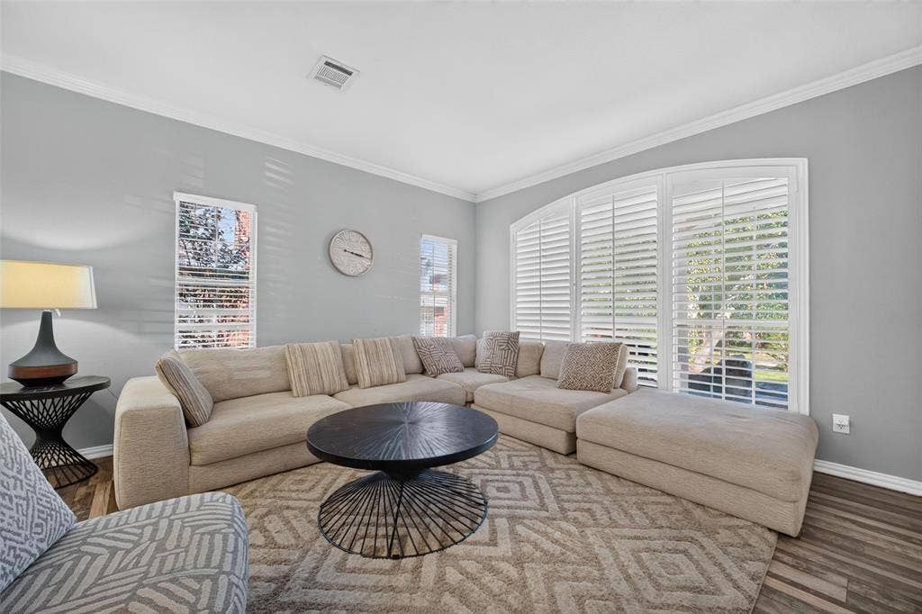 5726 Remington Drive, Garland, TX 75044 Neutral-toned living space featuring wood-finish flooring, crown molding, and an expansive arched window assembly equipped with integrated plantation shutters
