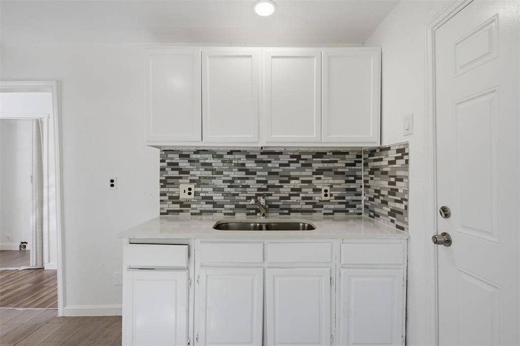 336 Bonnie View Road, Dallas, TX 75203 Kitchenette featuring white cabinetry, a neutral-toned countertop, a multi-tonal mosaic tile backsplash, and a drop-in stainless steel sink