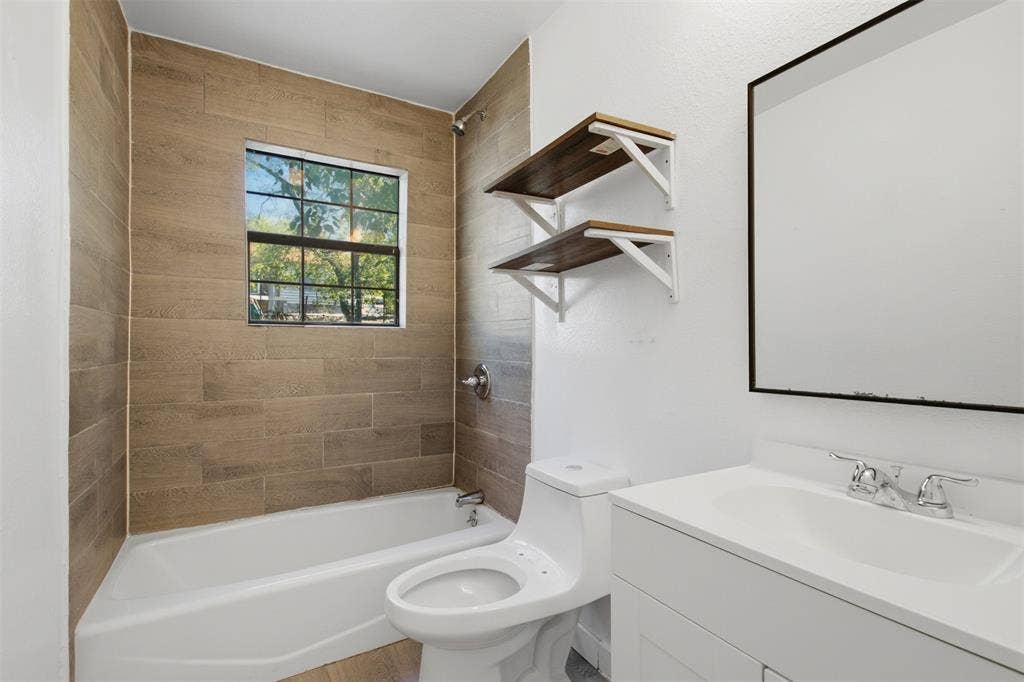 336 Bonnie View Road, Dallas, TX 75203 Bathroom featuring wood-finish tile shower surround, integrated vanity with an oval basin, wall-mounted tiered shelving, and a rectangular mirror with a black frame