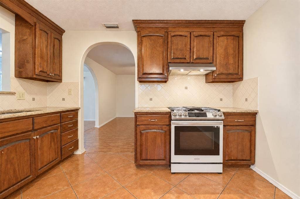 1910 R Avenue, Plano, TX 75074 Kitchen featuring raised-panel wood cabinetry, stone countertops, diamond-pattern tile backsplash, stainless steel gas range, and diagonal tile flooring