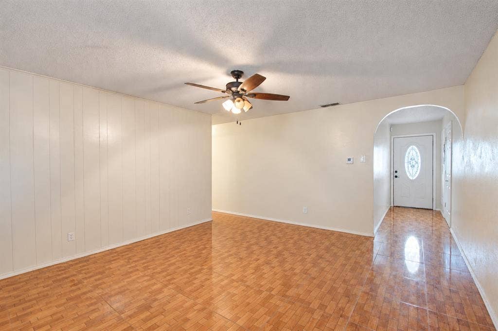 1910 R Avenue, Plano, TX 75074 Interior space featuring wood-finish flooring, a ceiling fan with multi-light fixture, vertical paneling, and an arched entryway with an exterior door containing an oval glass insert
