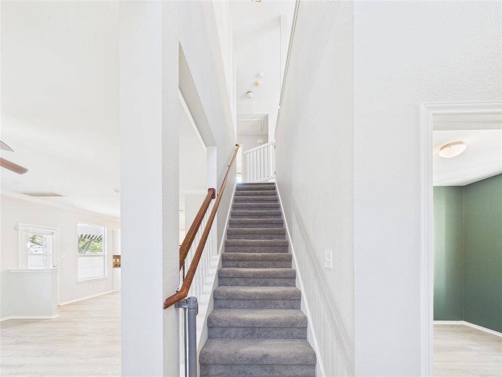 Staircase featuring carpeted steps, a wood-finish handrail, and white balusters, flanked by neutral wall finishes and wood-finish flooring