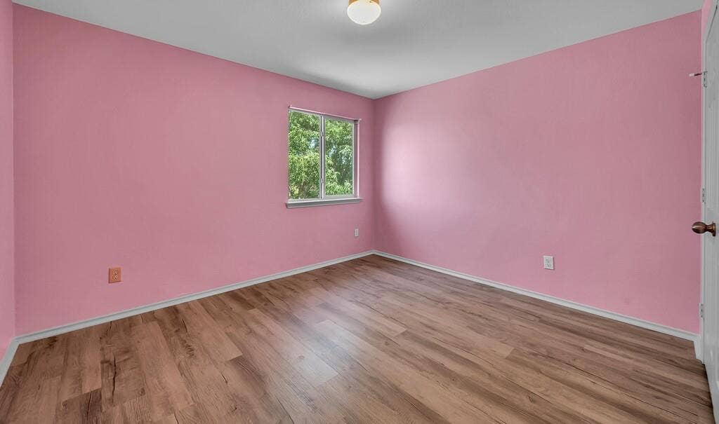 Wood-finish flooring, single window with exterior scenery, flush-mount ceiling lighting, and multi-panel interior door