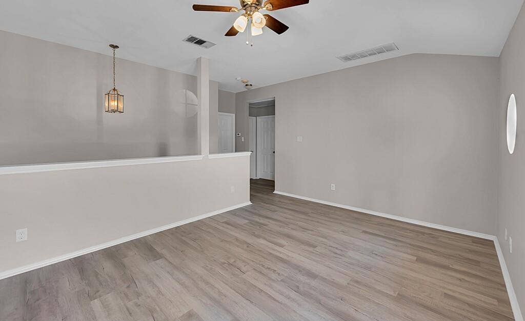 Vaulted ceilings, wood-finish flooring, half-wall partition, integrated ceiling fan with light fixture, and pendant lighting