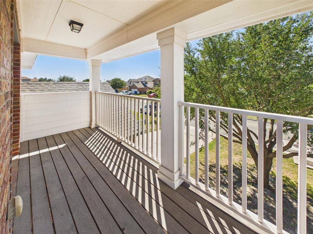 Covered balcony featuring wood-finish decking, white square columns, and a coordinating picket-style railing