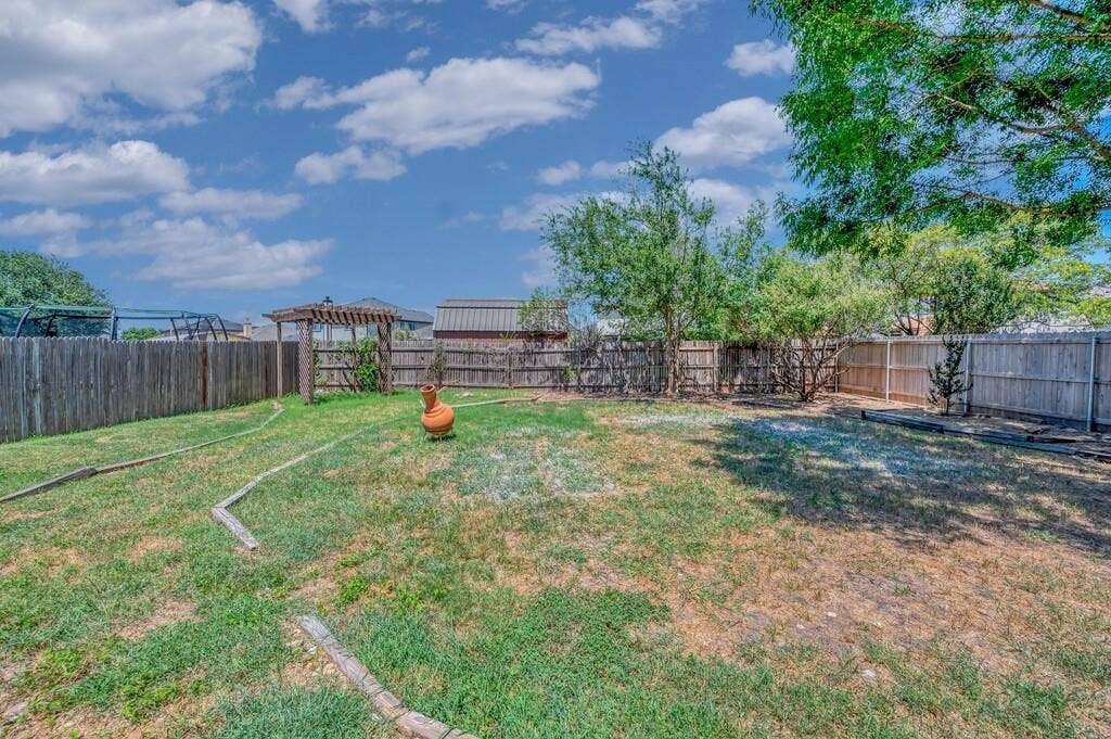 Fenced backyard featuring a wood pergola, mature trees, and natural landscaping borders