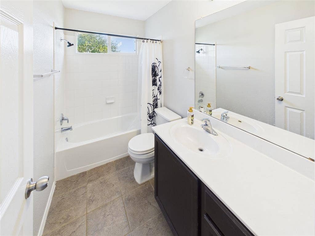 Upstairs Full bathroom featuring a dark-finish vanity with an integrated white countertop, a large wall-mounted mirror, a porcelain tub-and-shower combination, and tiled flooring