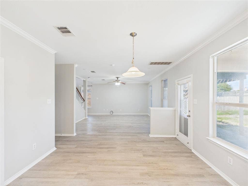 Dining/Living Area Neutral-toned interior featuring wood-finish flooring, crown molding, a hanging pendant light, a ceiling fan with light fixture, and a glass-paneled exterior door