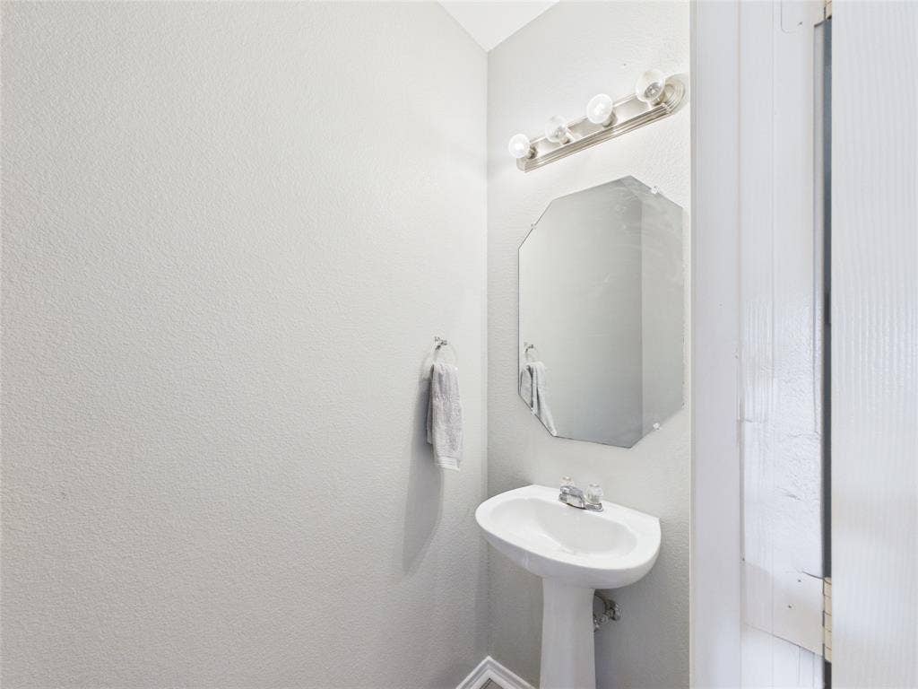 HALF BATH down stairs Pedestal sink with a dual-handle faucet, octagonal wall mirror, and four-bulb vanity lighting fixture