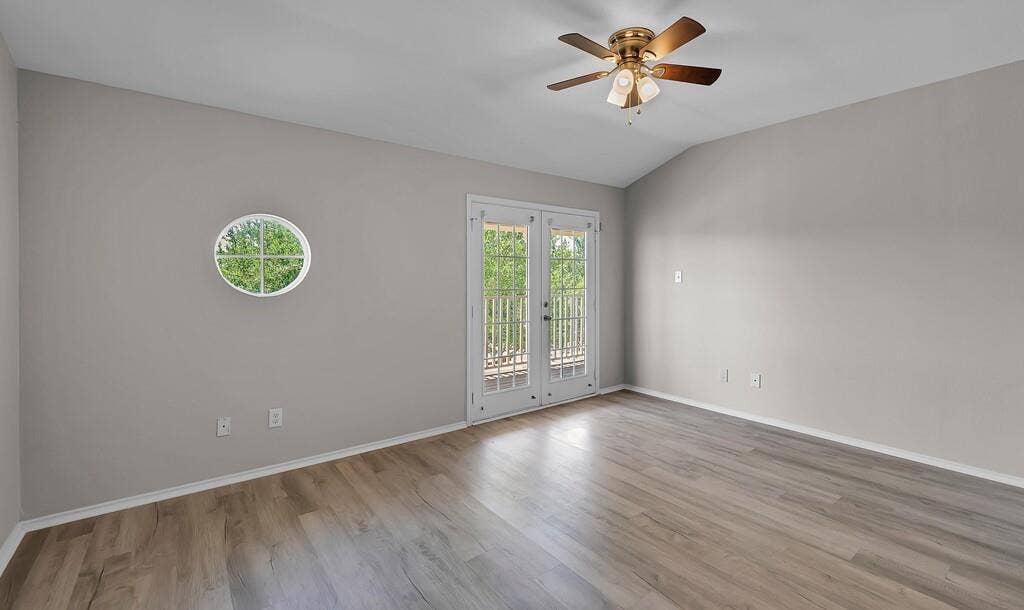 Vaulted ceilings, wood-finish flooring, circular accent window, glass-panel French doors, and ceiling fan with integrated lighting
