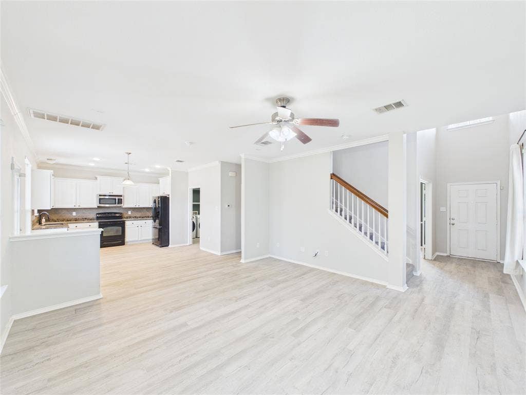 Open floor plan featuring wood-finish flooring, kitchen cabinetry with neutral-tone countertops, a ceiling fan, and a staircase with a wooden handrail