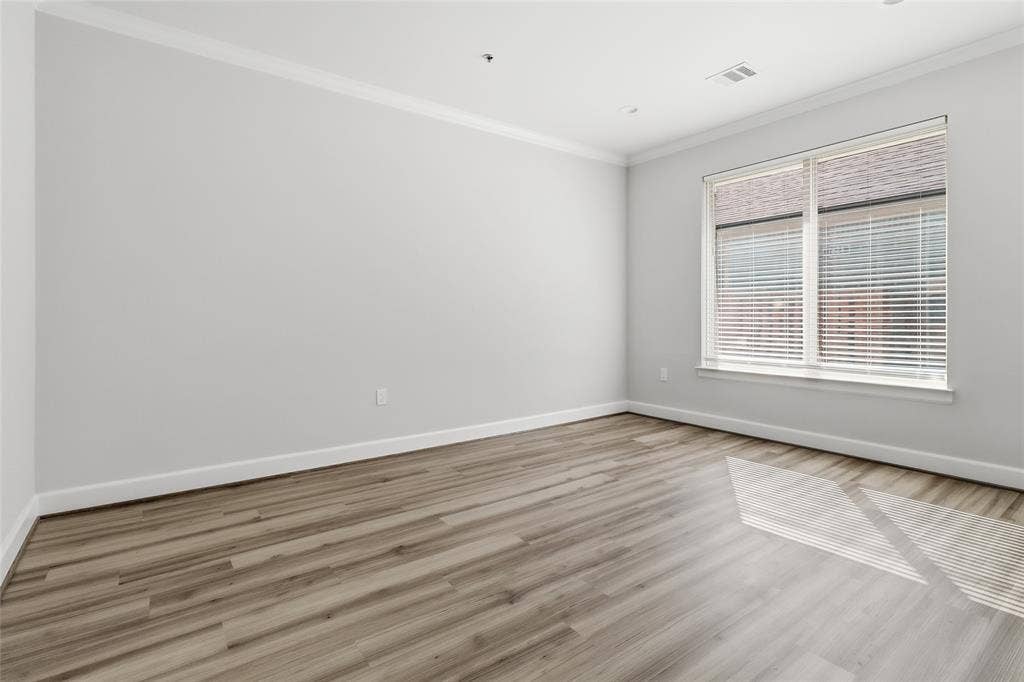 Neutral interior featuring wood-finish flooring, crisp crown molding, and large window with horizontal blinds