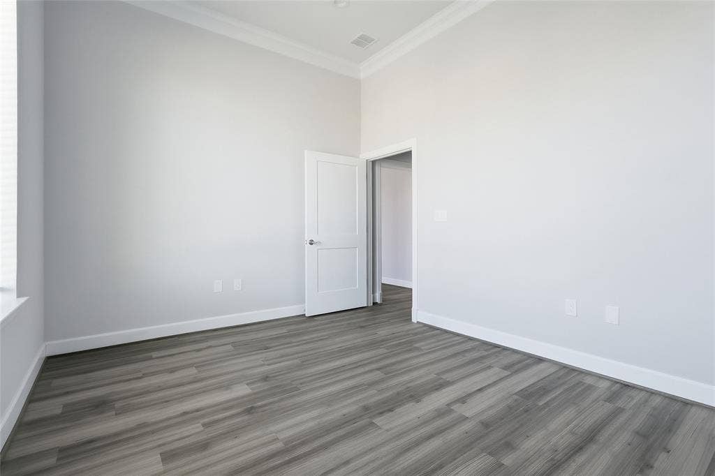 High-ceiling room featuring wood-finish flooring, crown molding, and a paneled interior door